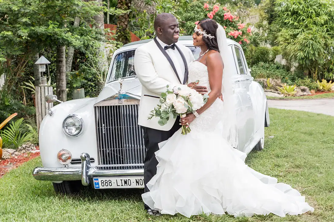 Bride and groom posing with a vintage Rolls-Royce on the lawn at the Bamboo Gallery wedding venue in Davie, Florida